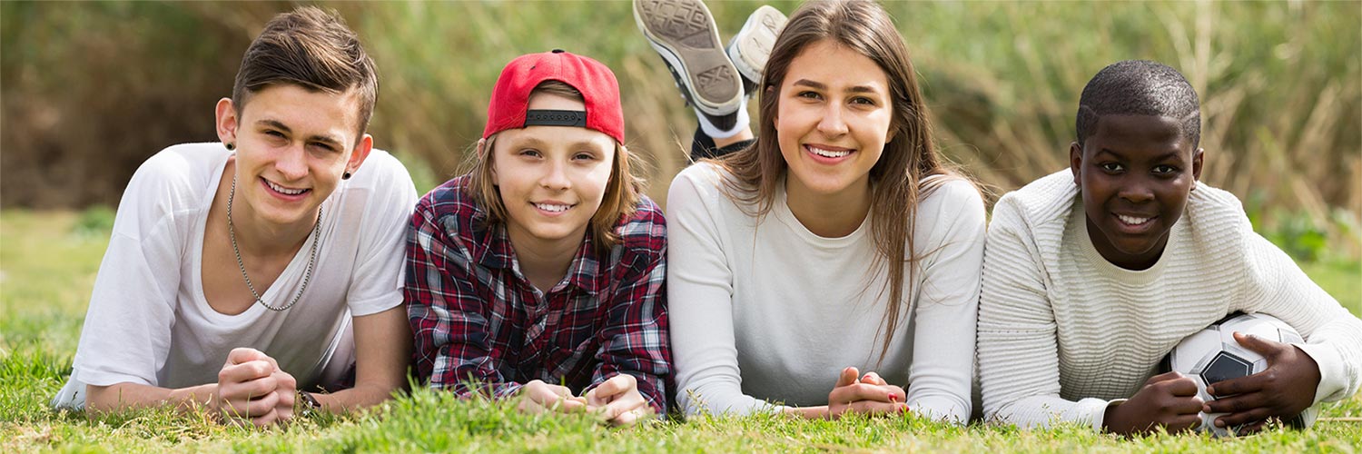 Four teens laying on their stomachs on the grass smiling.