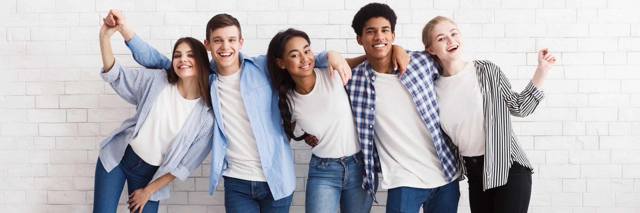 Group of teens standing, smiling and laughing with their arms over each other's shoulders.