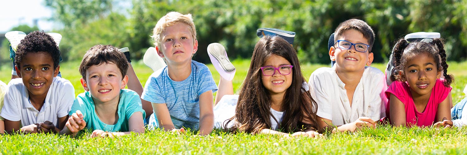 Kids laying on their stomachs on the grass smiling.