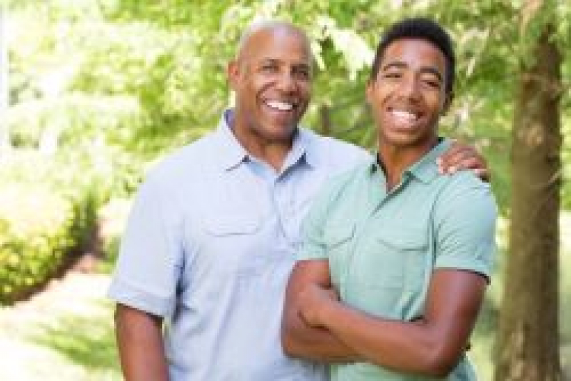 Father standing with his arm over his son's shoulders. Both smiling.